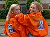 Zu sehen sind zwei junge DJV-Mitglieder am Rande eines WDR-Streiks. Sie tragen orange DJV-Jacken mit der Aufschrift "Journalismus ist mehr wert!". – 